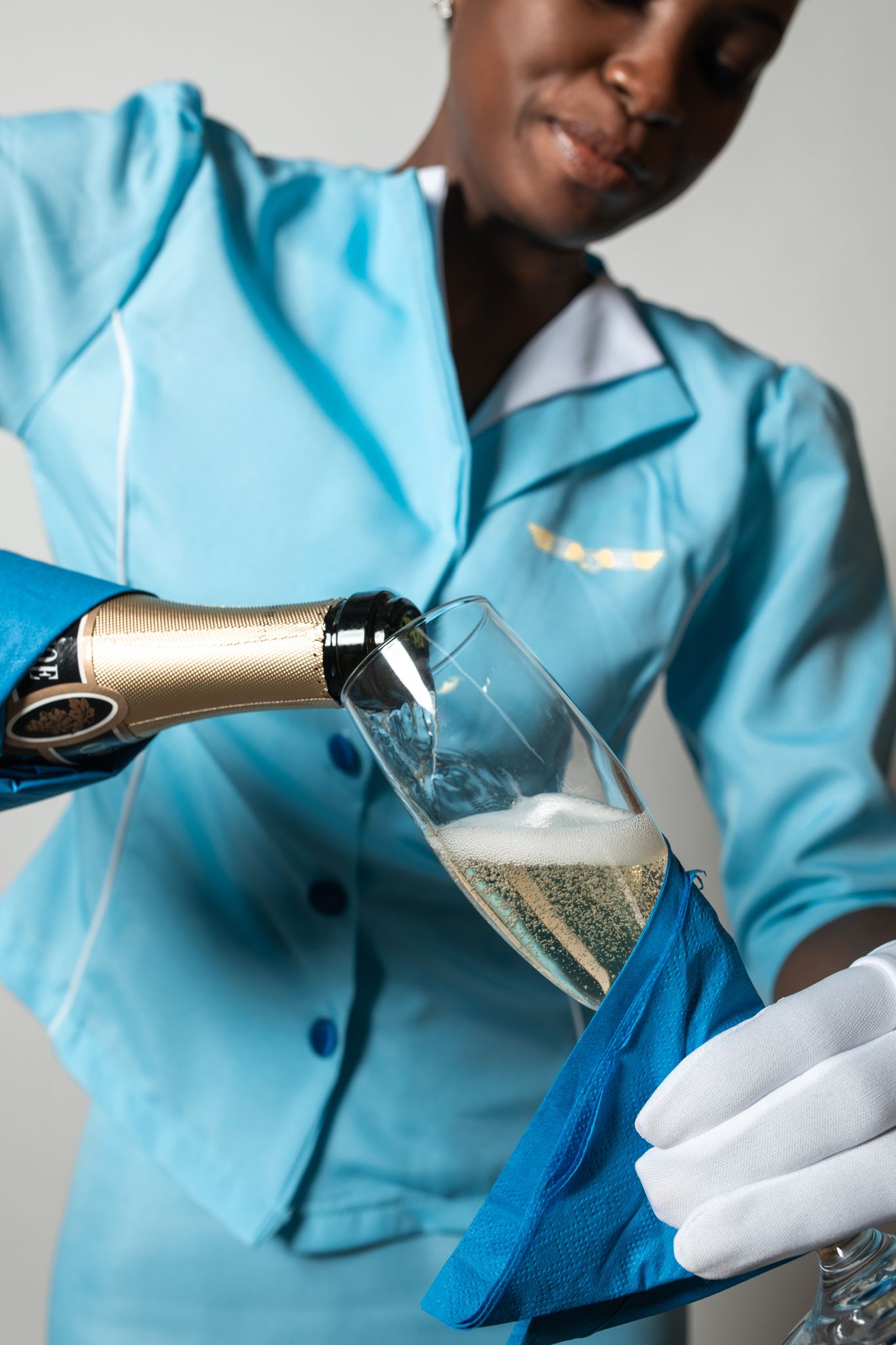 Close-up of a flight attendant in blue uniform pouring champagne into a glass.