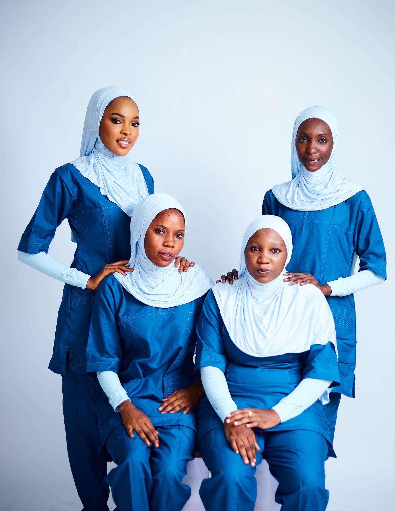 Four African nurses wearing hijabs and blue uniforms posing indoors.