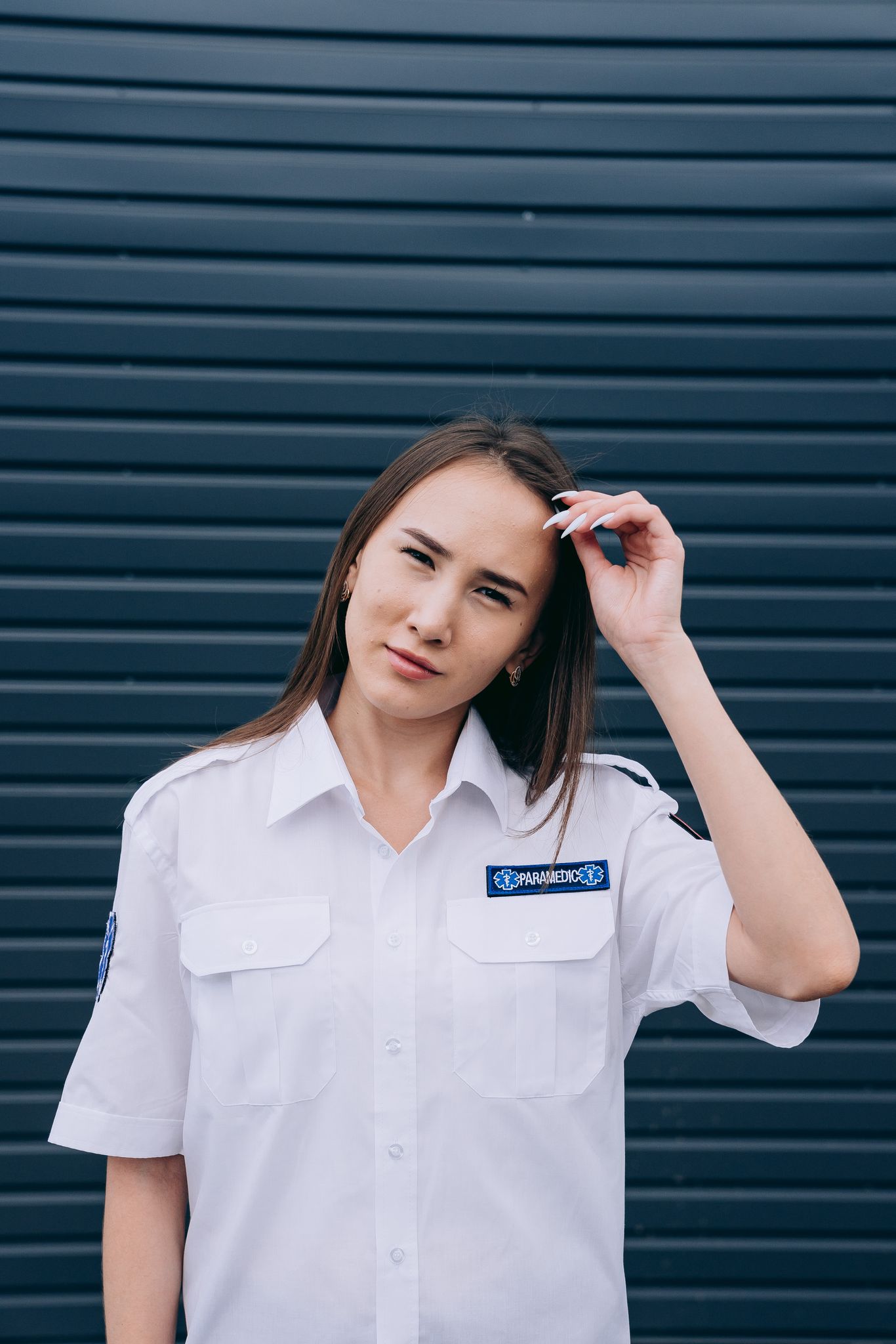 Portrait of a young female paramedic standing confidently in uniform against a dark backdrop.